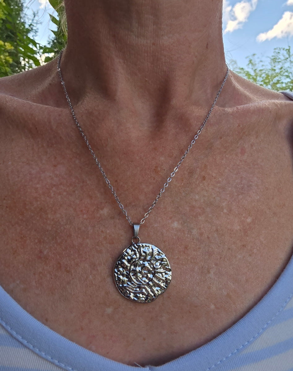 Person wearing a necklace with a detailed pendant against a natural background